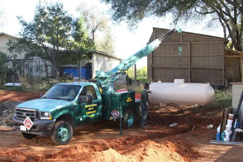 Crane truck setting a new propane tank on a property